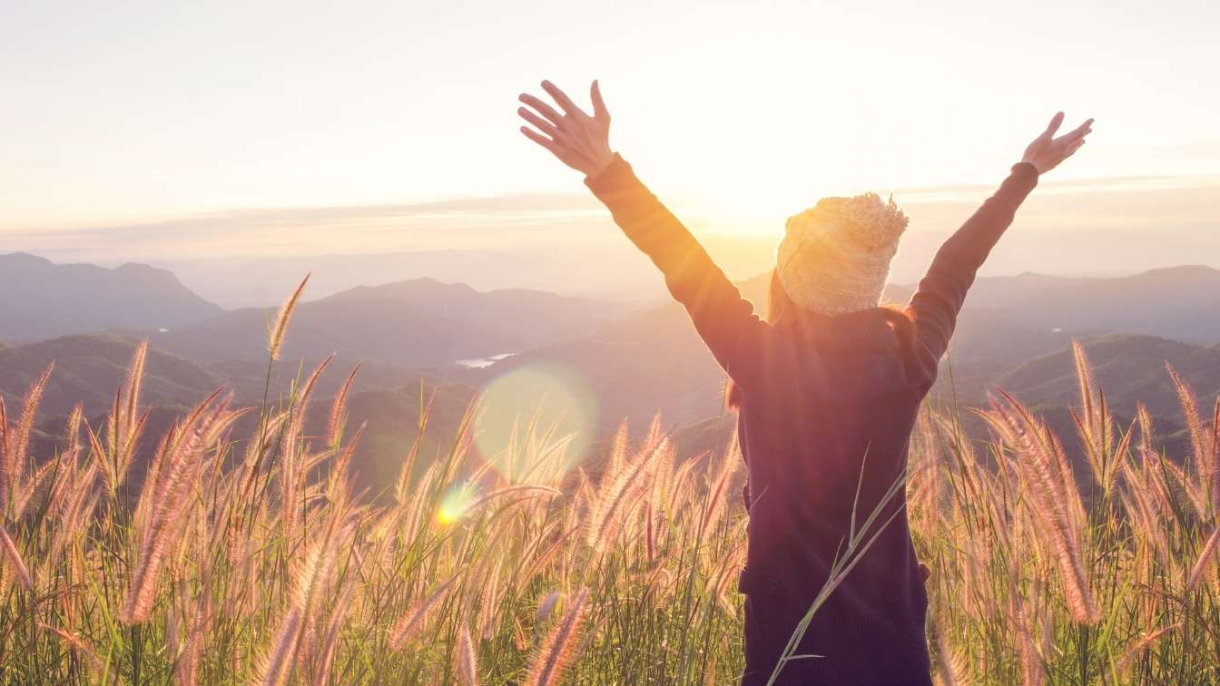 Woman in freedom pose in tall grass at sunrise