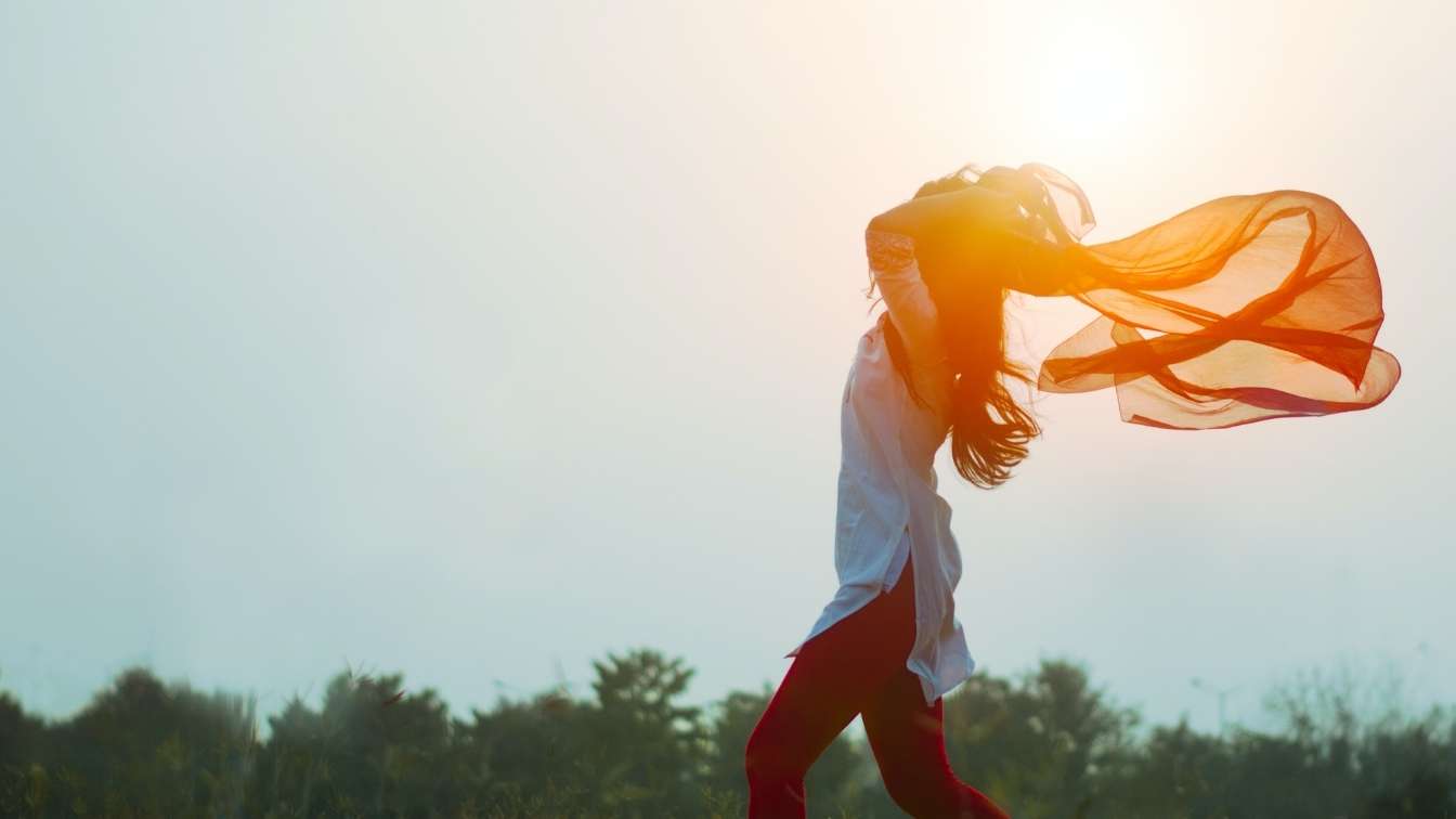 WOman with orange scarf trailing in breeze in freedom pose